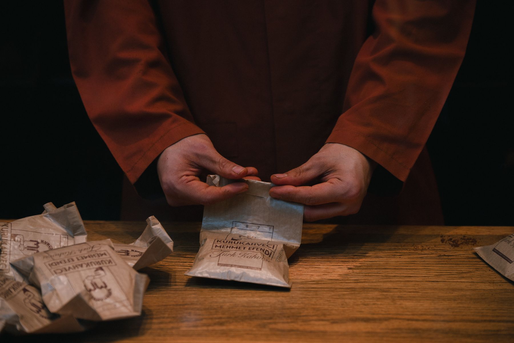 Un ouvrier scellant des sacs de café en papier sur une table de travail en bois